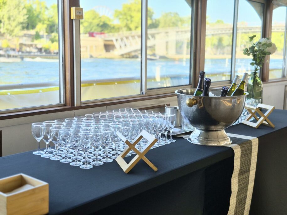 Buffet de verres et seau à champagne devant les baies d'un bateau, la Seine au soleil