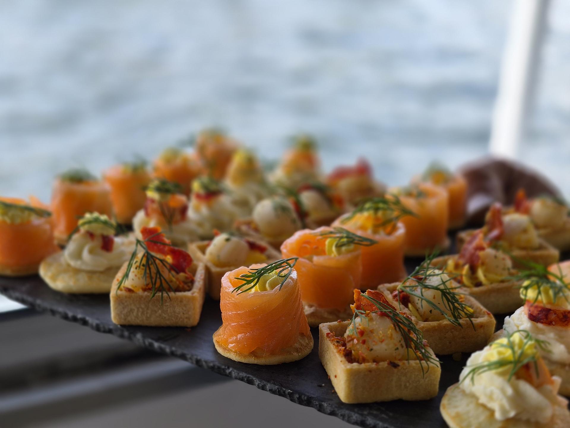 Canapés au saumon et tartelettes garnies sur une ardoise, la Seine au fond